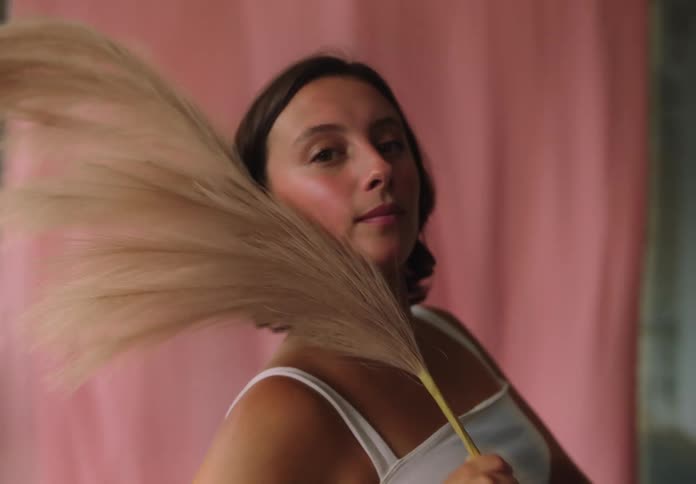 A young woman holding a feather fan standing and posing in front of a pink curtain
