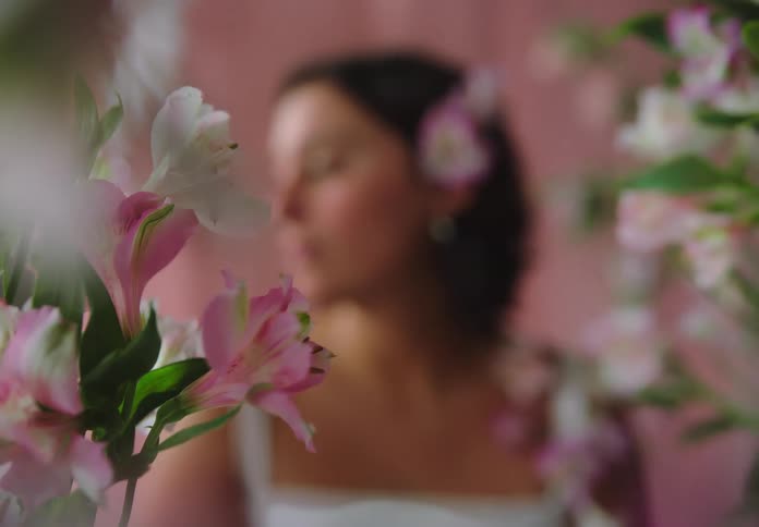 Young woman with a flower in her ear seen through a frame of white and pink flowers
