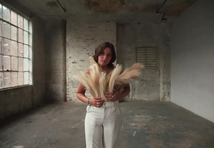 Woman poses wearing pampas grass styled as a dress in an industrial room