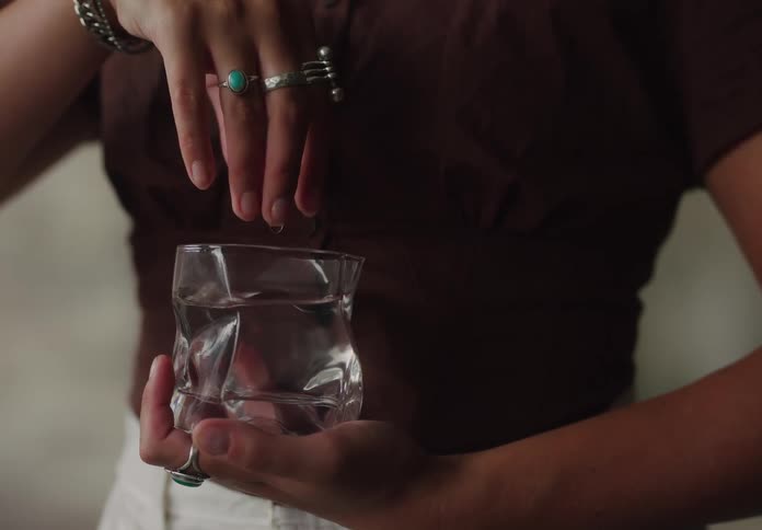 A woman wearing several rings on her fingers holds a glass of water and dips her finger into it