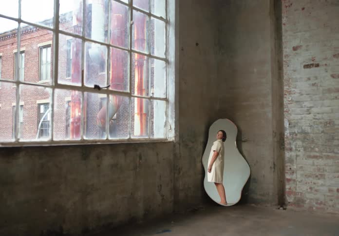 A young woman checking her dress in a mirror placed on the floor inside a building at midday