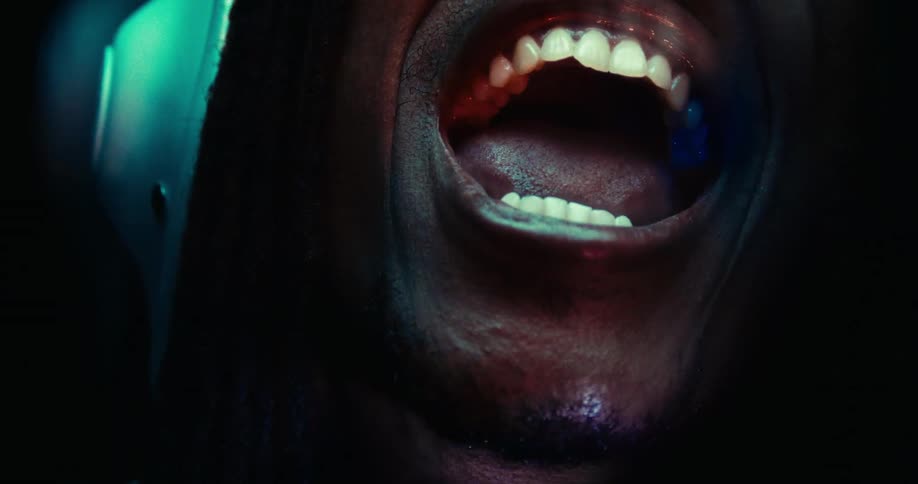 A black man with a large mouth and white teeth is yelling while wearing a helmet