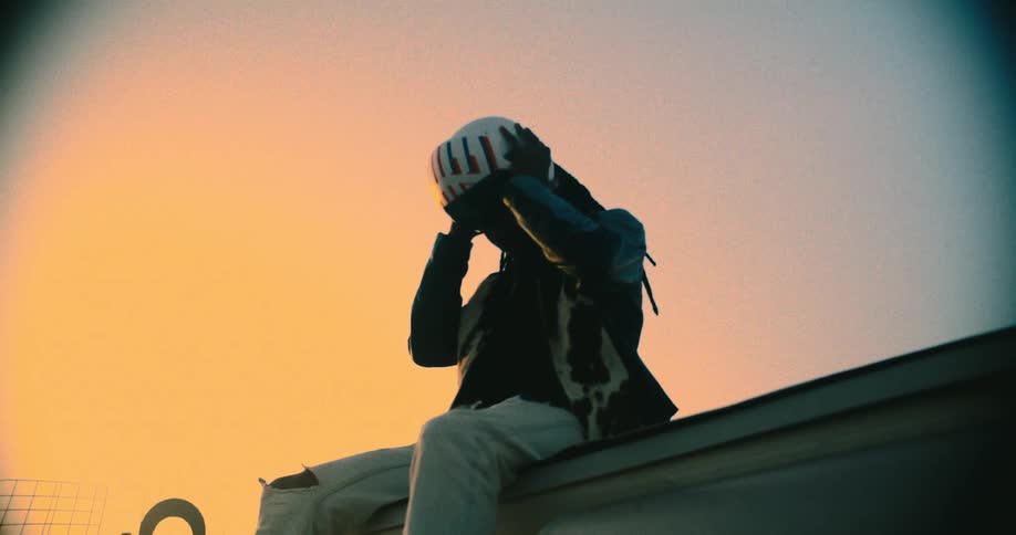 Dreadlocked man sitting outdoors taking off a white helmet