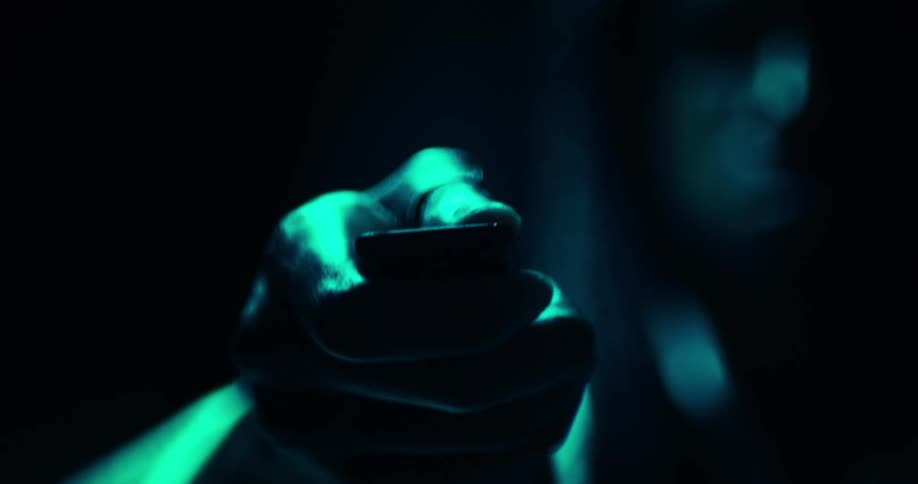 A hand illuminated in teal light points or holds something toward the camera