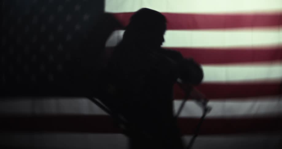 Silhouette of a person with a chair banging against a background of an american flag