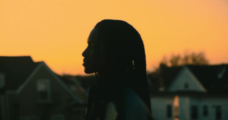 Silhouette of a man with dreadlocks in the foreground and urban houses in the background