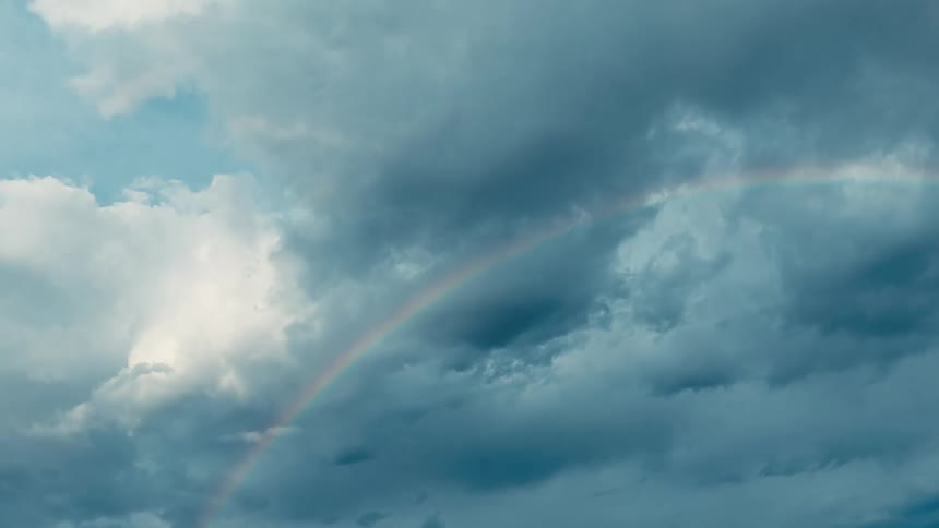A cloudy midday sky with a rainbow stretching across it