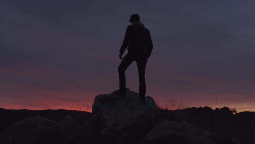 Silhouette of a man climbing on top of a rock in an outdoor setting at dawn