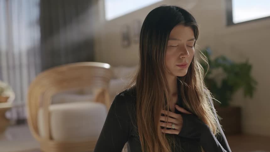Woman sitting with her hand on her chest and her eyes closed taking a deep breath