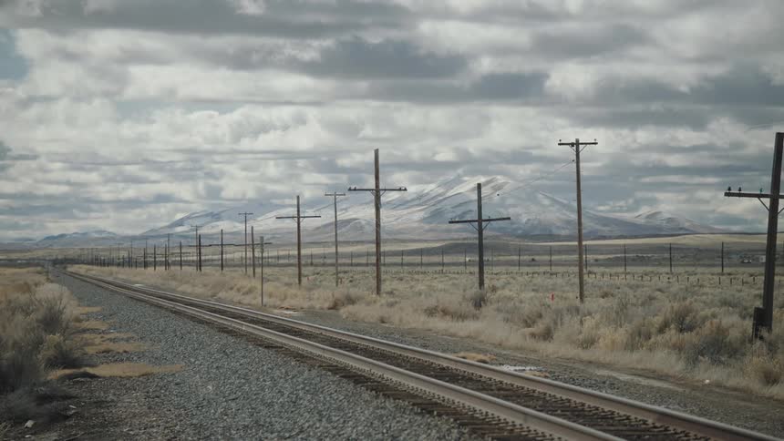 A railway line running through the countryside with utility poles lining the tracks at midday