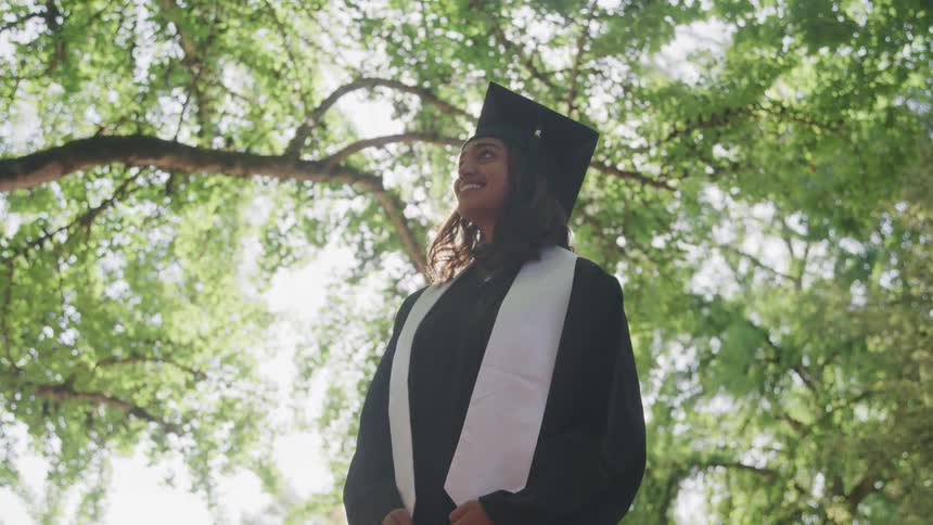 Smiling young woman with graduation gown in an outdoor setting with trees