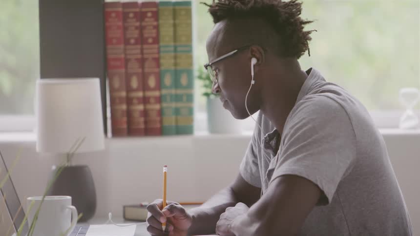 Man interacting with a laptop and writing while sitting at a table