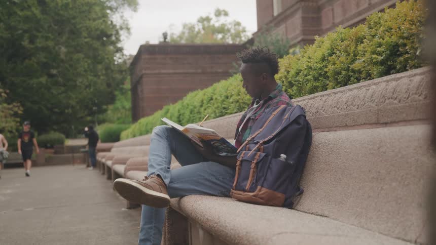 Young man sitting on a stone bench outdoors writing on a notebook