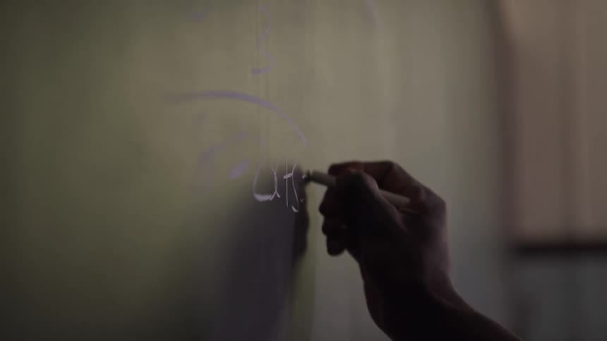 The person is writing with chalk on the chalk board