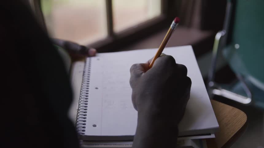 Person in classroom with a pencil writing in a notebook
