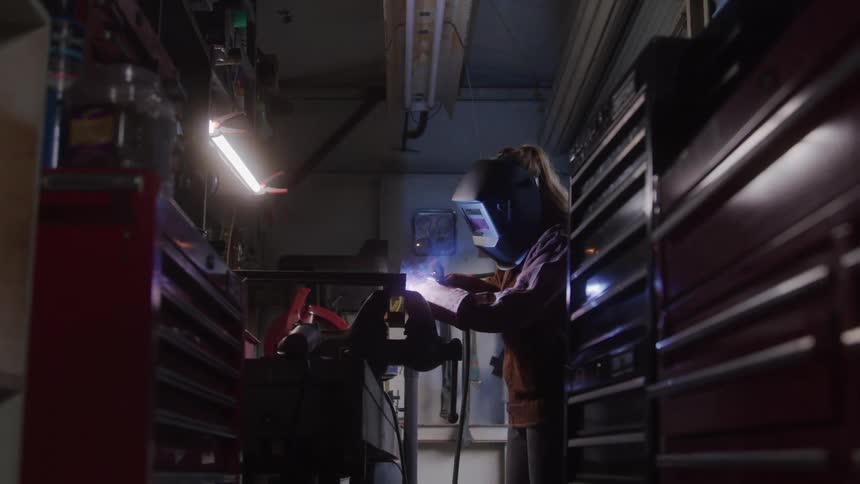 Woman putting on a mask and welding an object in a workshop