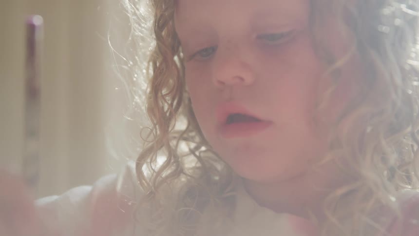 Little girl with curly hair playing with a paintbrush