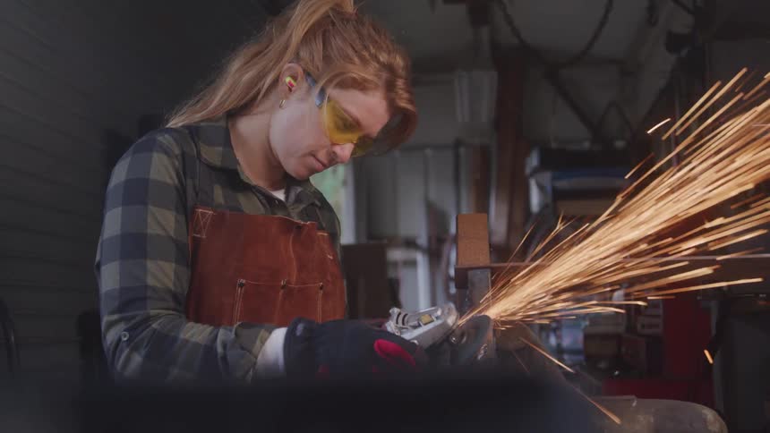 The woman is grinding metal and shooting sparks all over