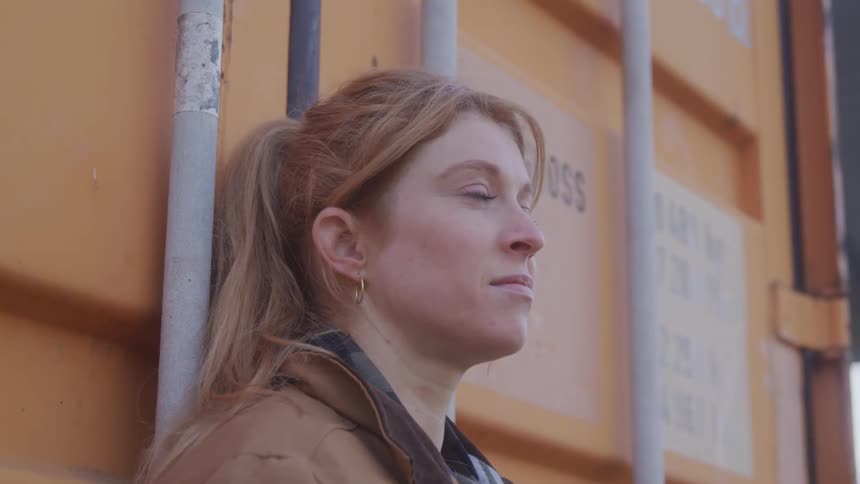 Blonde woman leaning against an orange metal area outdoors