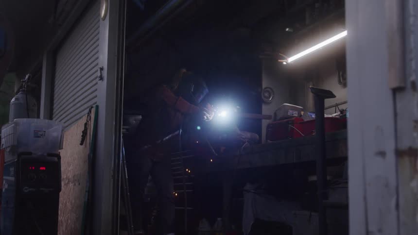 Indoor shot of a workshop with a person with a welding helmet engaged in welding