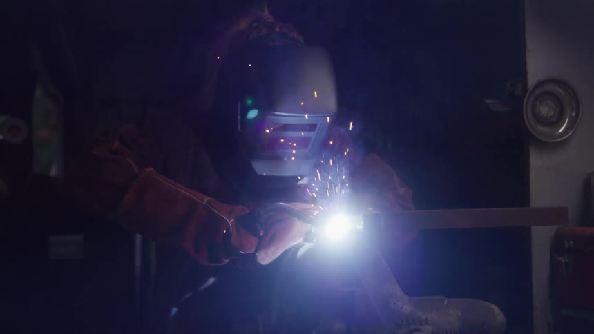The video features a welder in a dark environment wearing a protective helmet and gloves engaged in welding a bright arc of light illuminates the metal being joined indicating an active and focused industrial task