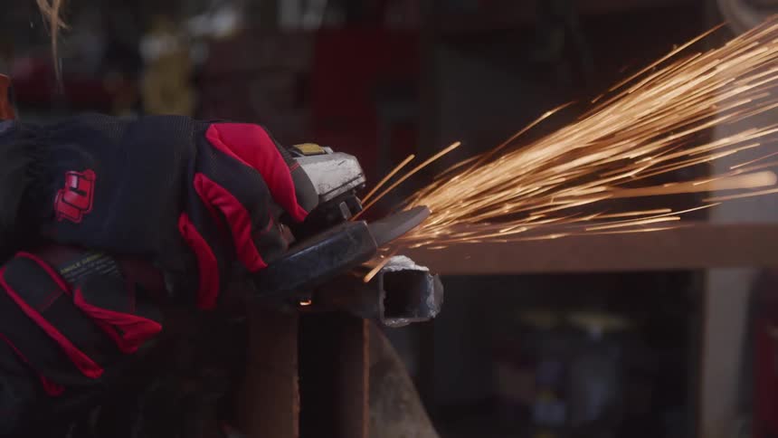 Gloved hands using a chainsaw on a piece of metal