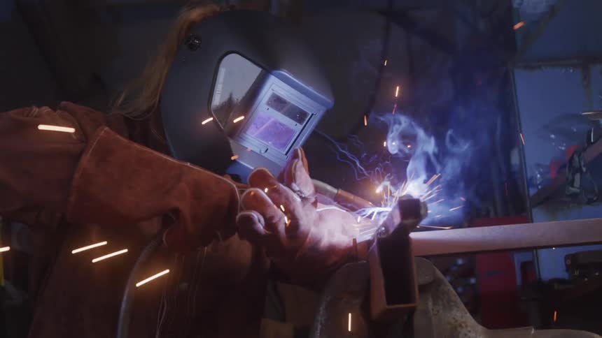 Woman with gloves and handling a tool and welding with sparks coming out