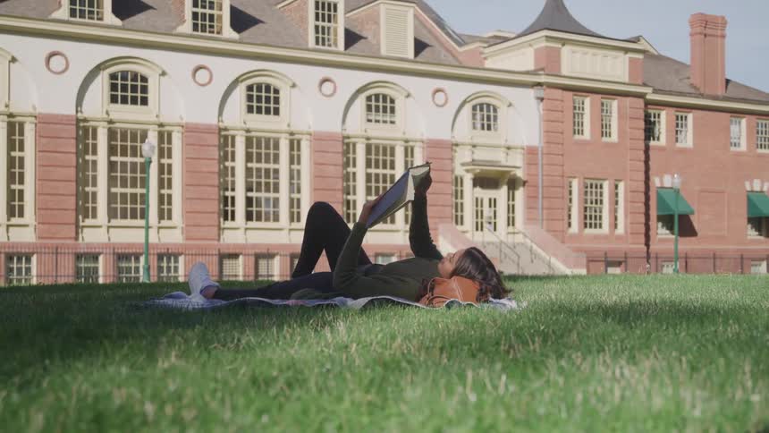 Woman lying on a cloth in the grass reading a book