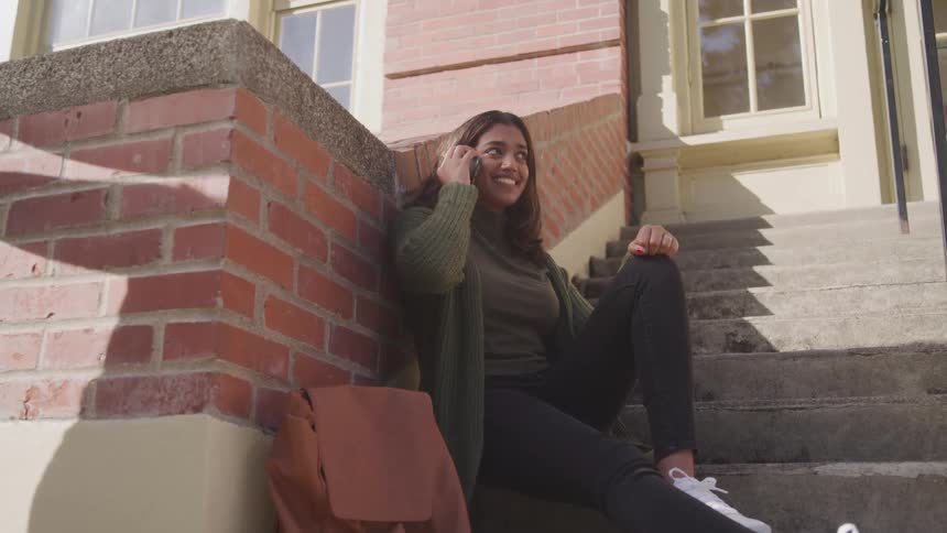The woman is sitting on the steps talking on her phone