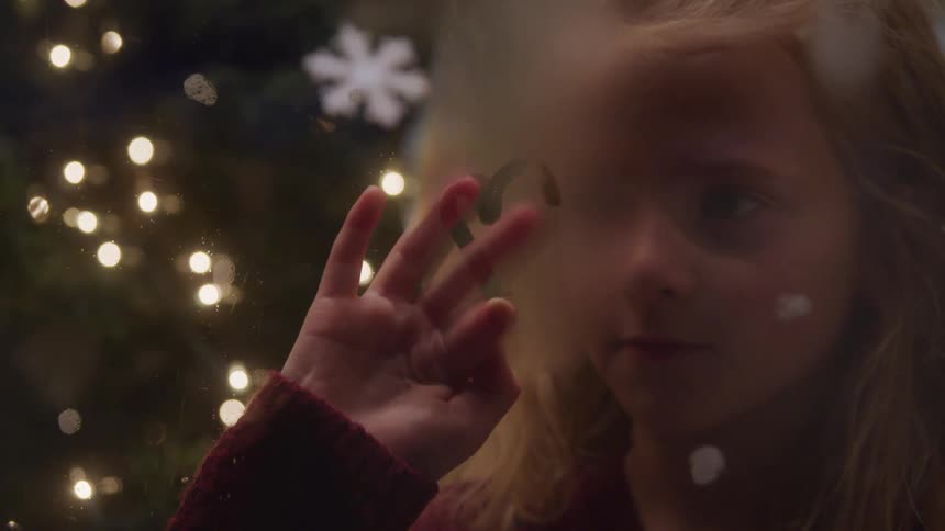 Little girl drawing on a foggy window at snowy night