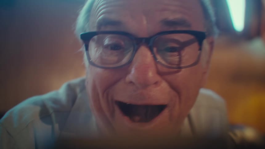 Elderly man with glasses in front of a smartphone vibrating happily