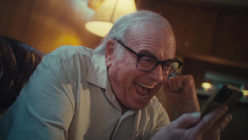 The man cheers and jumps in his seat while looking at his cell phone