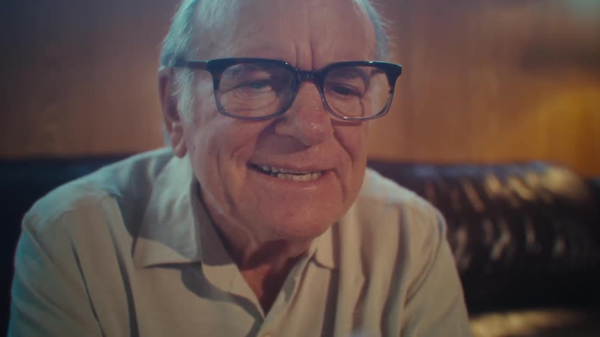 Man sitting on a leather couch smiles as he swipes on his phone