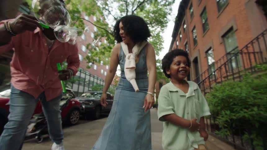 The video shows an adult and a young child possibly a father and son playing with a bubble wand on a city sidewalk the child is excitedly trying to catch the bubbles as they float through the air