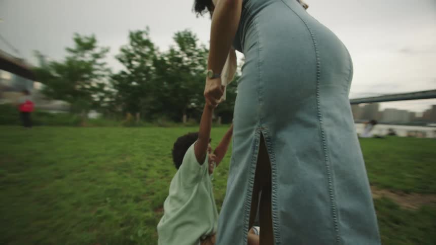 Mother plays with her son in a riverside park while a bridge towers in the background