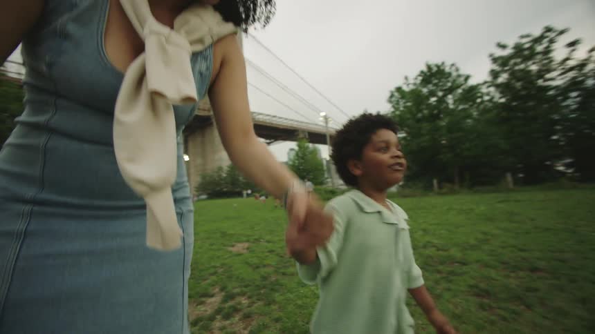 Mother and son happily walk together in a park near a large bridge