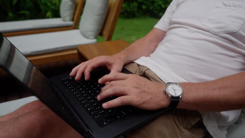 Man sitting in one chair in a row of lounge chairs types on a laptop
