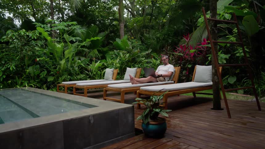 Man sitting poolside is typing on his laptop