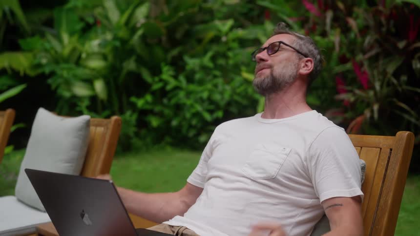 Man reacts angrily as he uses his laptop while sitting outdoors during daytime