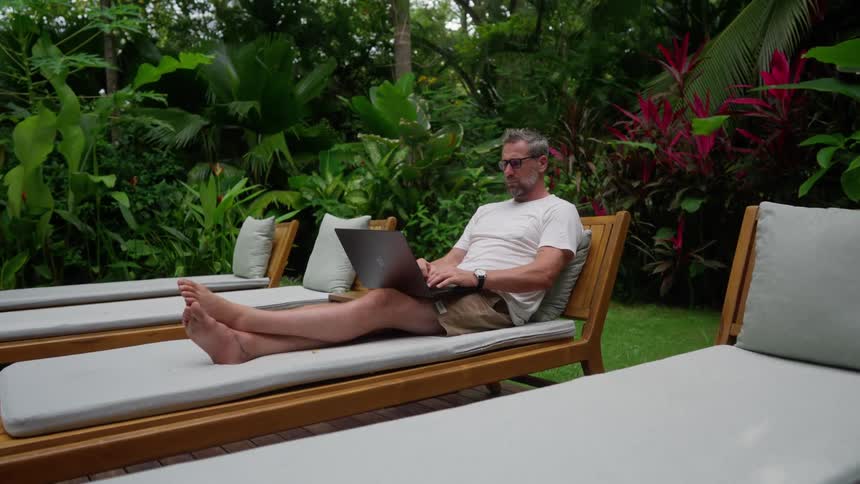 A man uses his laptop while sitting on a chair outdoors during daytime