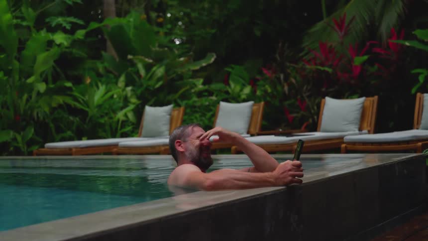 Man relaxes in a resort pool while talking on a video call