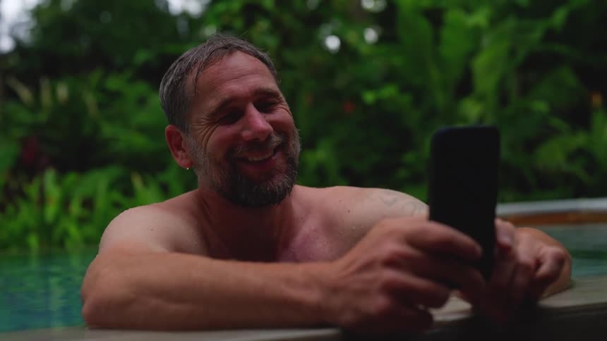 Smiling man interacting with a smartphone while standing in a swimming pool