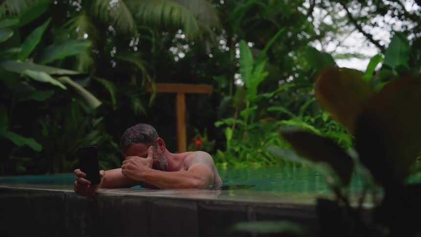 Man in the pool laughs while talking on the phone