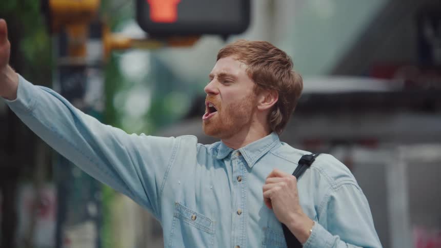 A young man screams and demonstrates while standing on a busy street outdoors during daytime