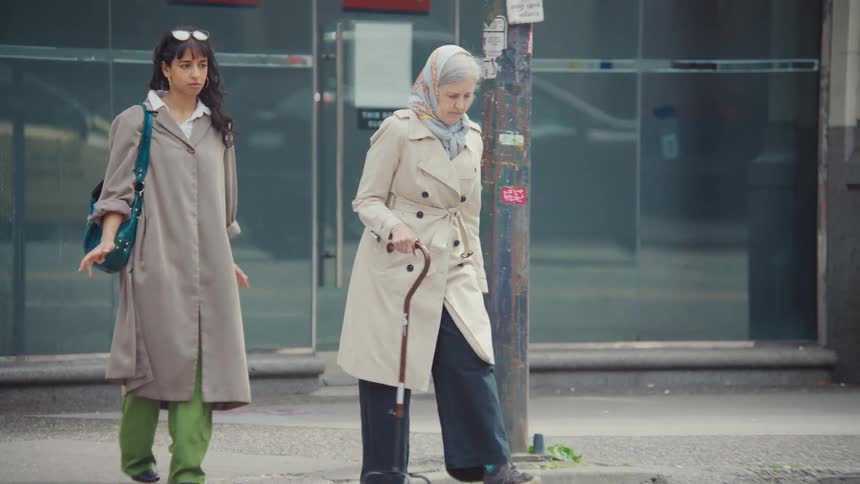 Female pedestrian blocked by a slow moving elderly woman hurries around her while they both cross a city street