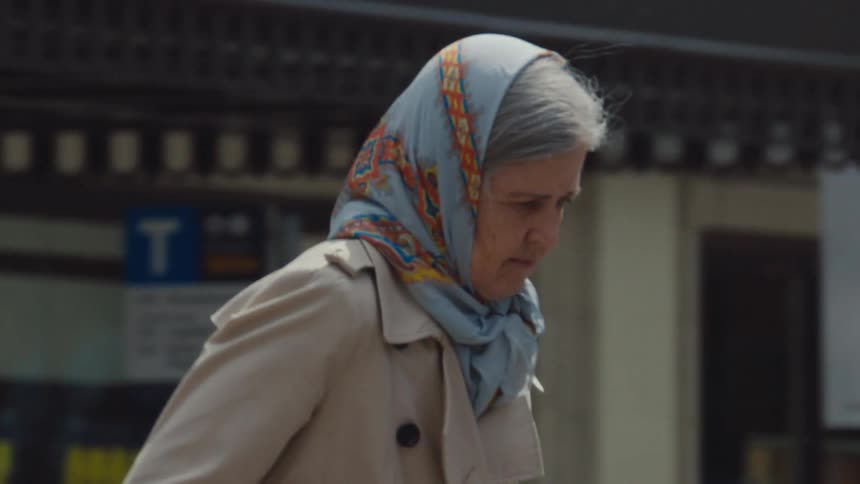 Elderly woman walks along a busy city street during daytime