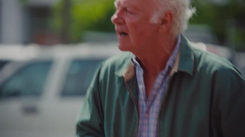 An angry elderly man pushing a shopping cart outdoors angrily talking to someone on the street at midday