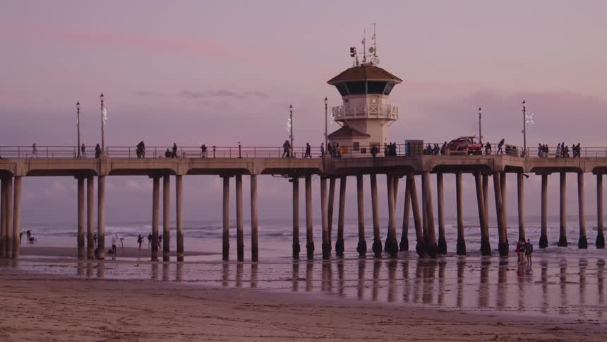 The iconic huntington beach pier in huntington beach at evening with a group of people walking back and forth along the bay