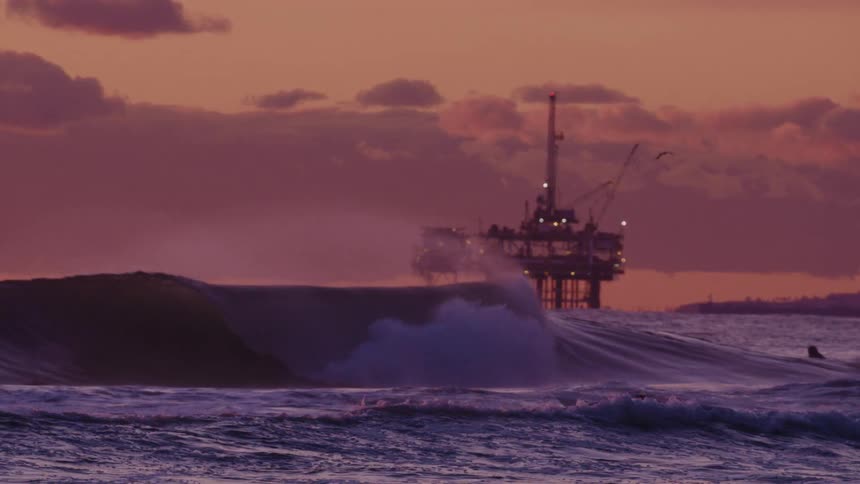 A footage of people surfing the sea with an oil island in the background