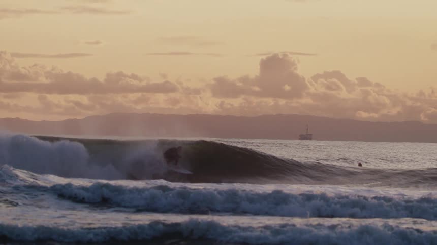 Surfer rides the large wave while two swimmers enjoy the water nearby